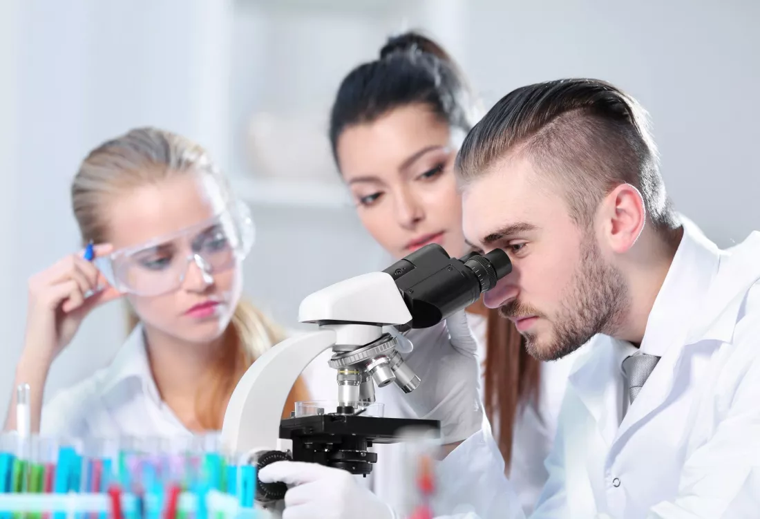 Młodzi laboranci w fartuchach pracują przy mikroskopie w laboratorium.